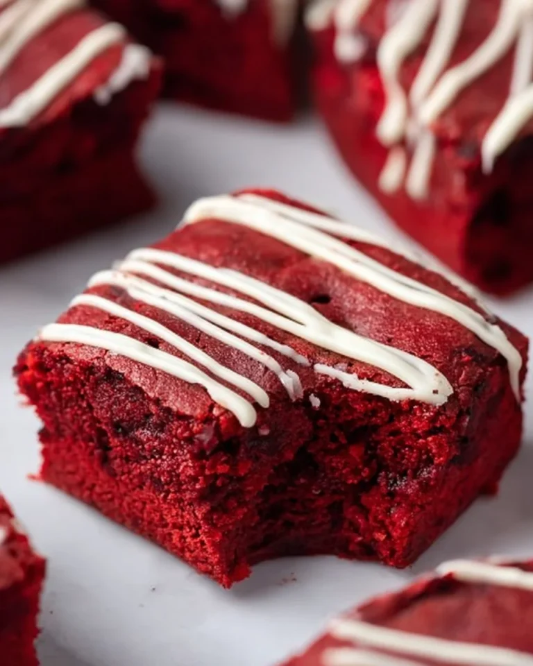 Fudgy red velvet brownies topped with cream cheese frosting on a plate.