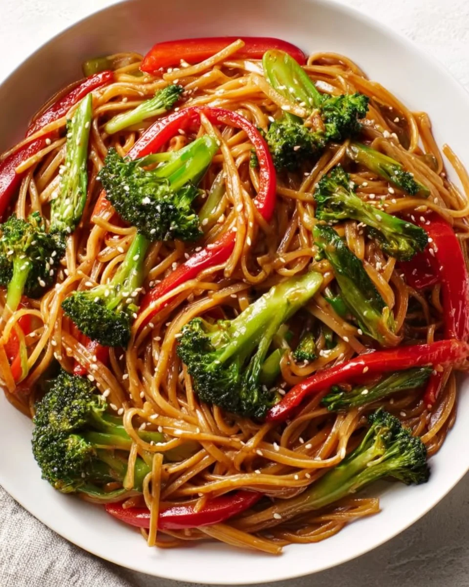 A colorful serving of vegetable lo mein topped with fresh vegetables and soy sauce.