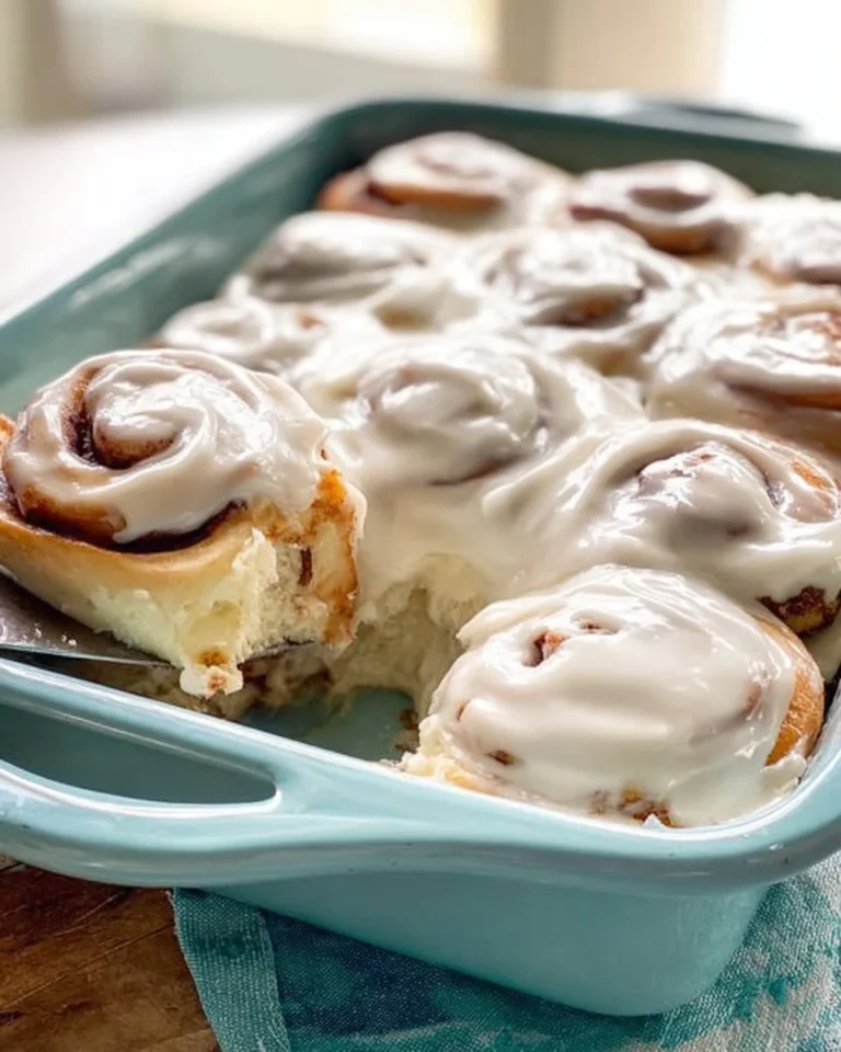 Freshly baked cinnamon rolls topped with sweet icing on a wooden table.